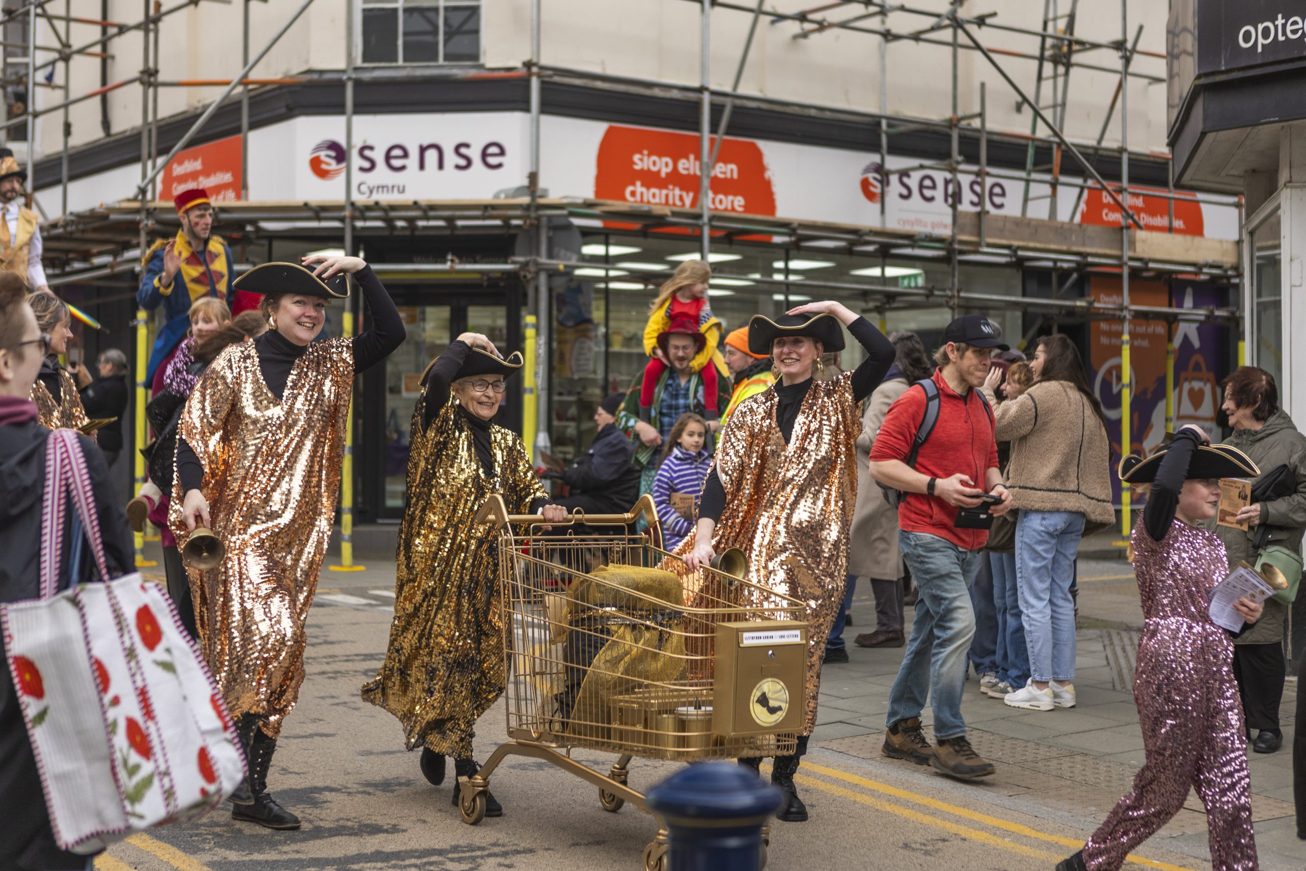 A group of female town criers in gold sequinned cloaks and tricorn hats process through the streets of Aberystwyth